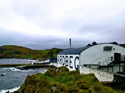 Weiße Ardbeg-Gebäude mit großem Schriftzug unmittelbar an der felsigen Küste.