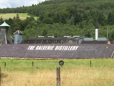 Balvenie-Brennereigebäude mit Pagodendach vor grünen Feldern und bewaldeten Hügeln.