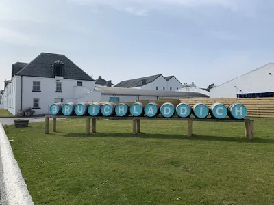 Weiße Bruichladdich-Gebäude hinter einem türkisfarbenen Brennereischriftzug.