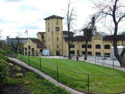 Helle Four-Roses-Gebäude mit Turm und grünem Vorplatz.