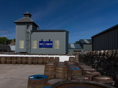 Kilchoman-Gebäude mit Pagodendach, blauem Schild und Fässern im Hof.