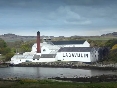 Weiße Gebäude der Lagavulin-Brennerei mit großem Schriftzug an der Bucht auf Islay.