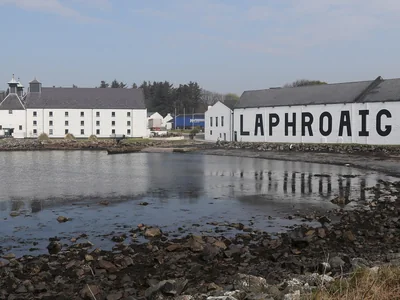 Weiße Laphroaig-Gebäude mit großem Schriftzug und Spiegelung im Küstenwasser.