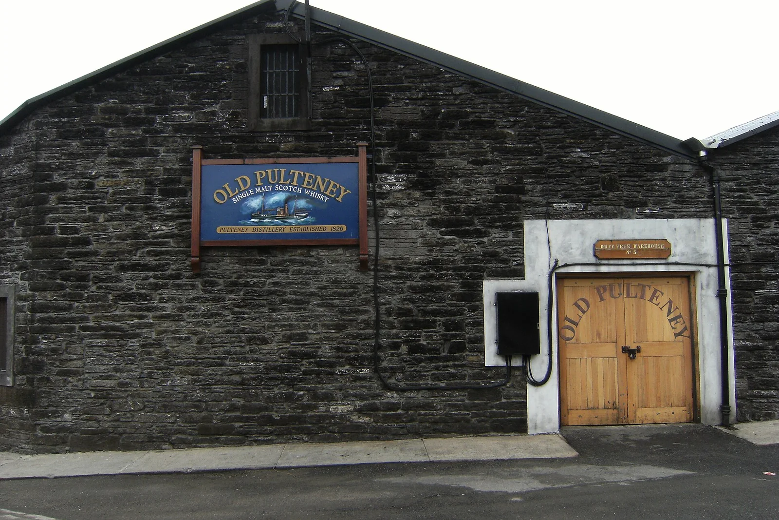 Steinerne Old-Pulteney-Fassade mit blauem Schild und Holztor.