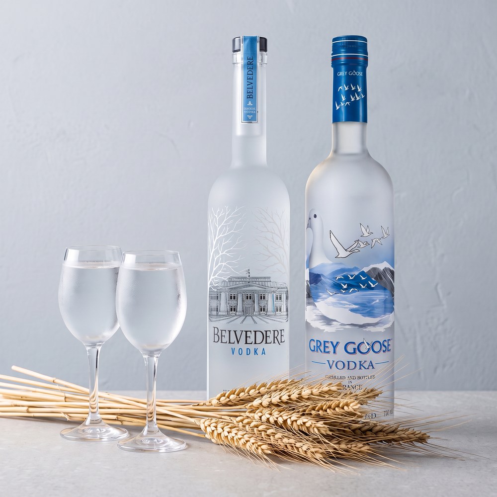 Belvedere und Grey Goose Vodka mit zwei Gläsern und Getreideähren auf heller Steinplatte
