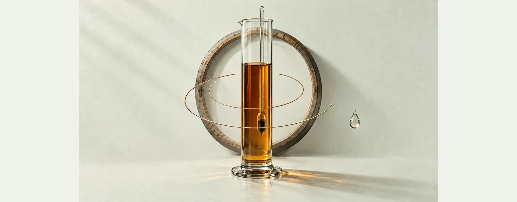 Ein Hydrometer steht in einem mit Whisky gefüllten Messzylinder, umgeben von zwei unterschiedlich großen Messbögen und einem Eichenring.